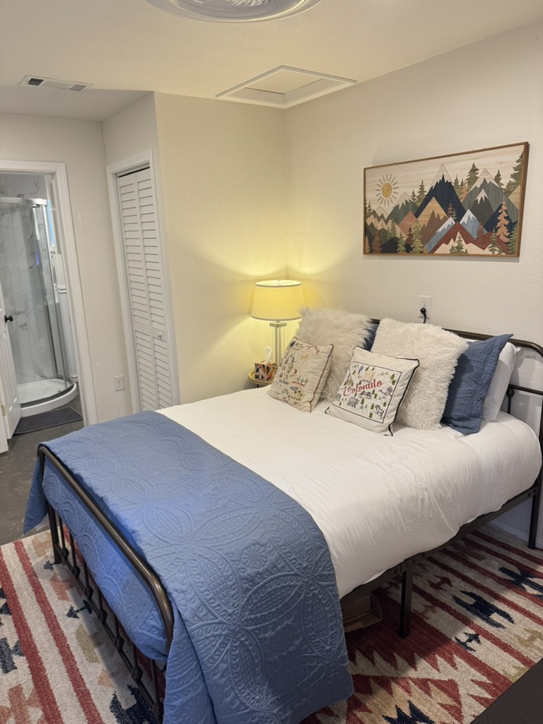 Guest bedroom with a queen bed, mountain artwork and an adjoining bathroom with a corner shower