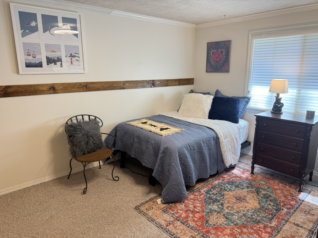 Bedroom with ski-lift artwork, a wood accent rail, antique dresser and a Persian rug
