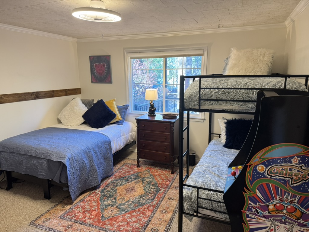 Bunk room with a twin bed, black metal bunk beds, Persian rug and a stand-up Galaga arcade cabinet