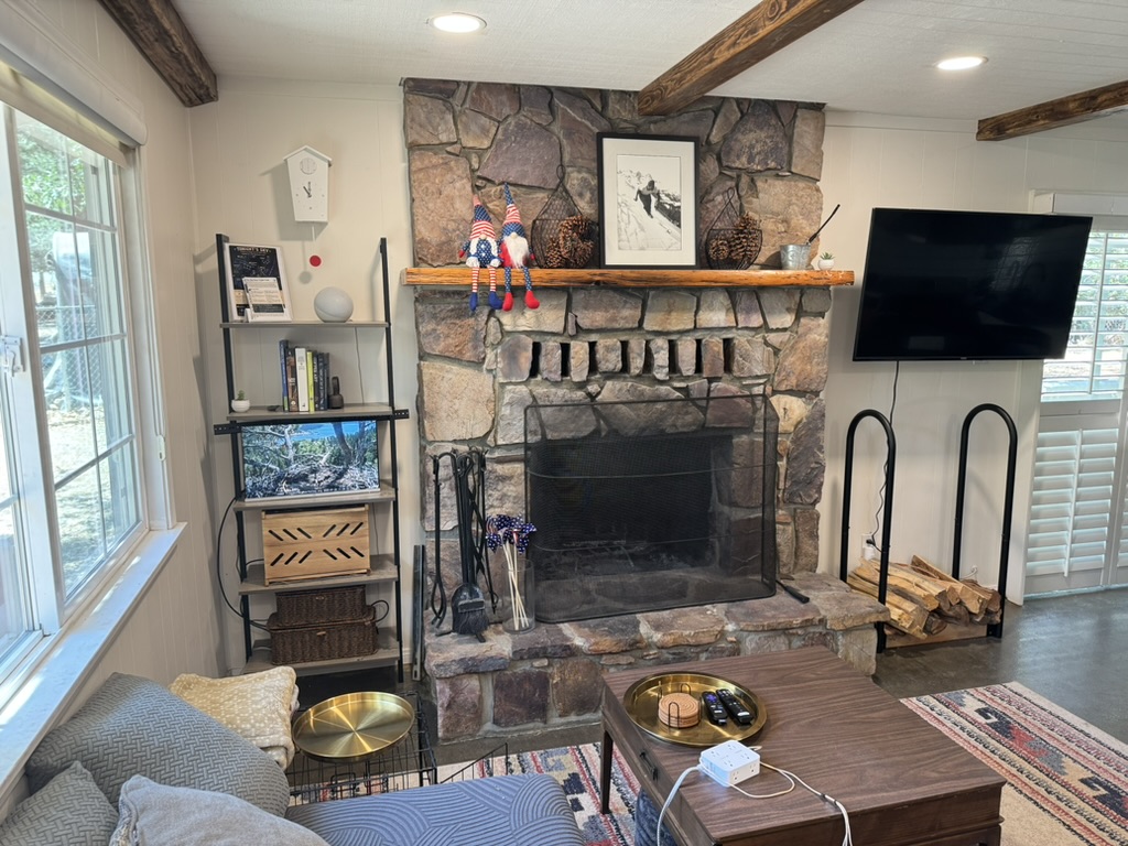 Close view of the stone hearth with a stacked log rack, fireplace tools and the eagle cam monitor on the shelf beside it