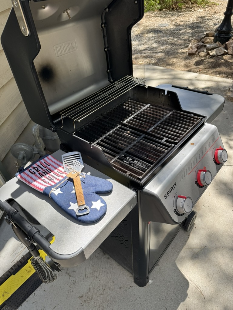 Weber Spirit gas grill open and ready with grilling tools, mitt and towel on the side table