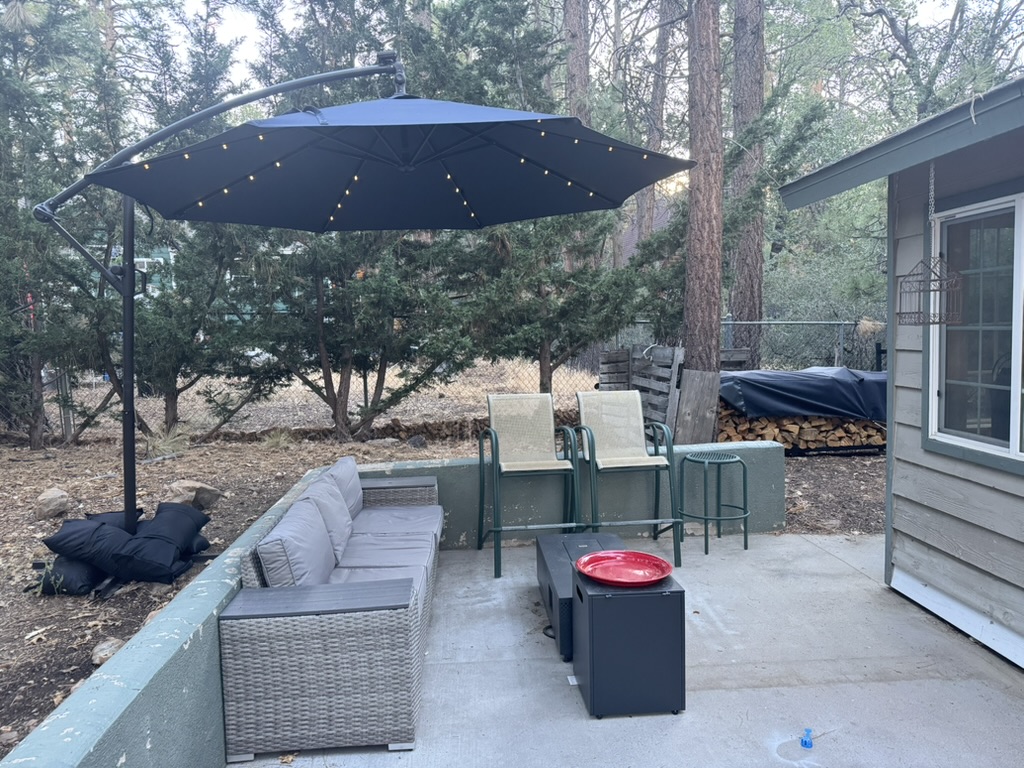 Patio at dusk with a cantilever umbrella lit by string lights, wicker sectional, fire table and a stacked woodpile
